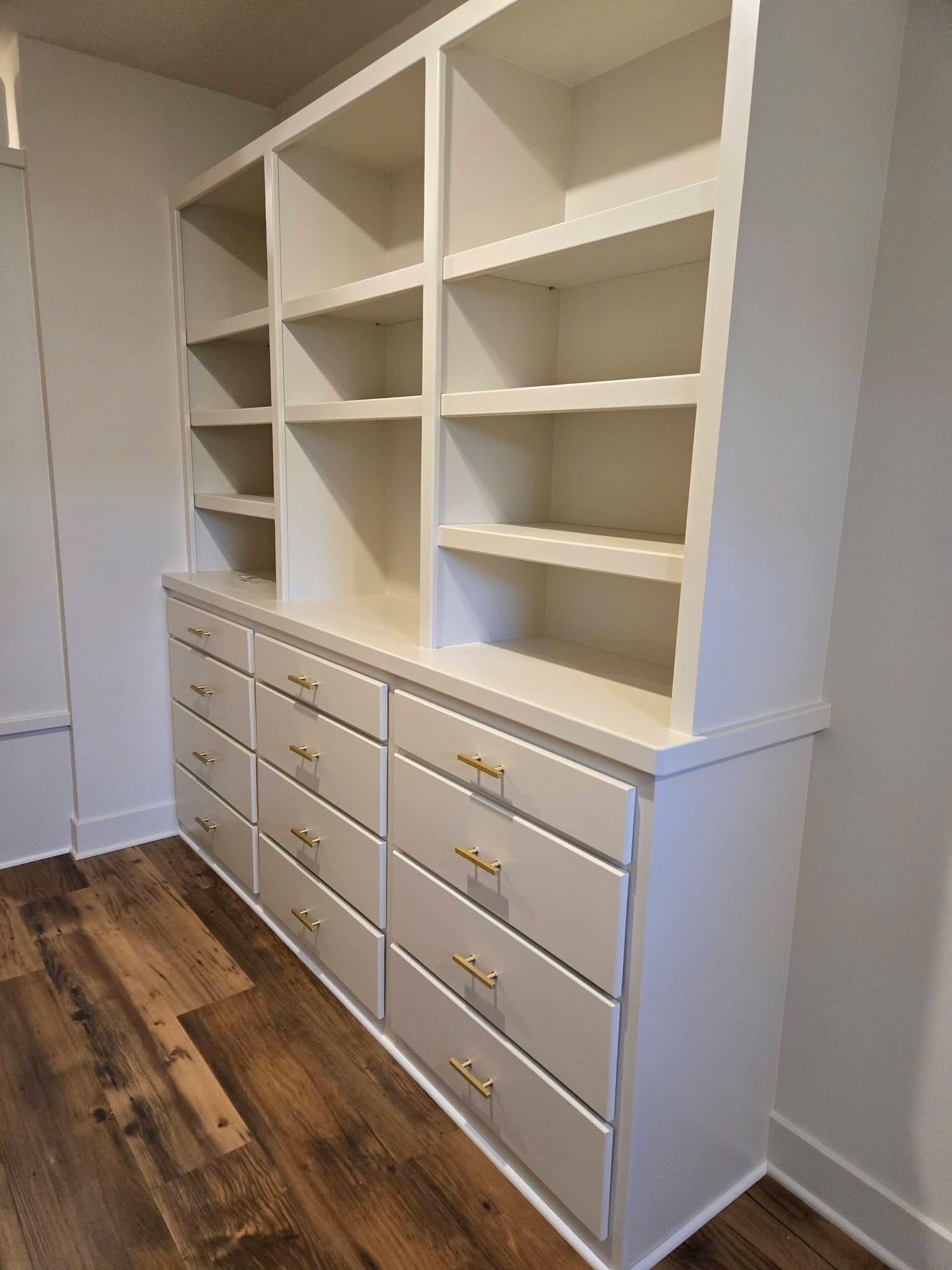 White built-in drawers with brass-colored handles and open shelving above.