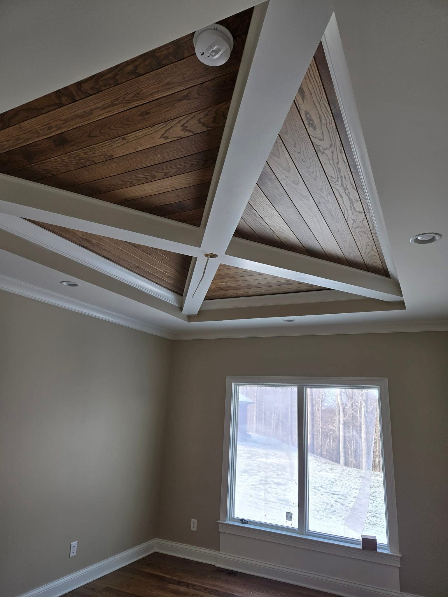 Wood plank ceiling panels framed by white crossing beams and perimeter molding.